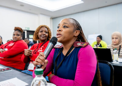 A woman speaks into a microphone from her seat at a desk while others look on.